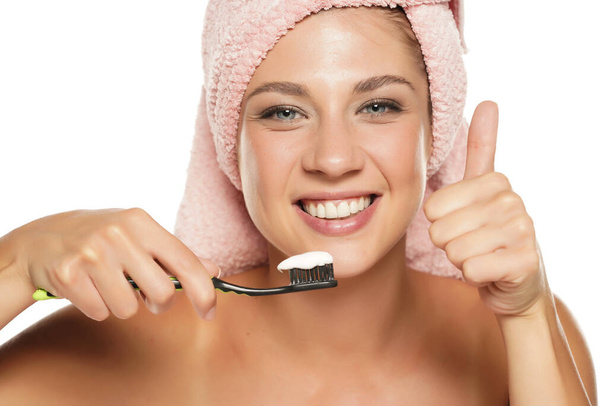 heureuse jeune femme tenant brosse à dents avec dentifrice sur fond blanc et montrant pouces vers le haut - Photo, image