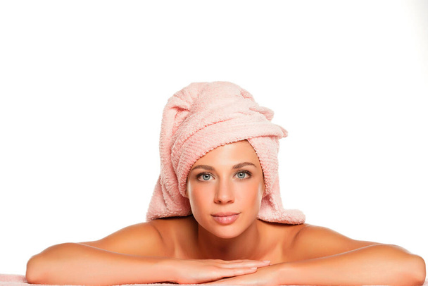 Молодая улыбающаяся красивая женщина позирует с полотенцем на голове на белом фоне - Фото, изображение