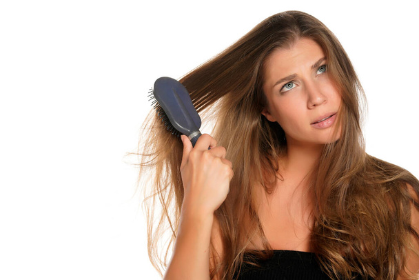 Молодая нервная женщина расчесывает волосы расчёской на белом фоне - Фото, изображение
