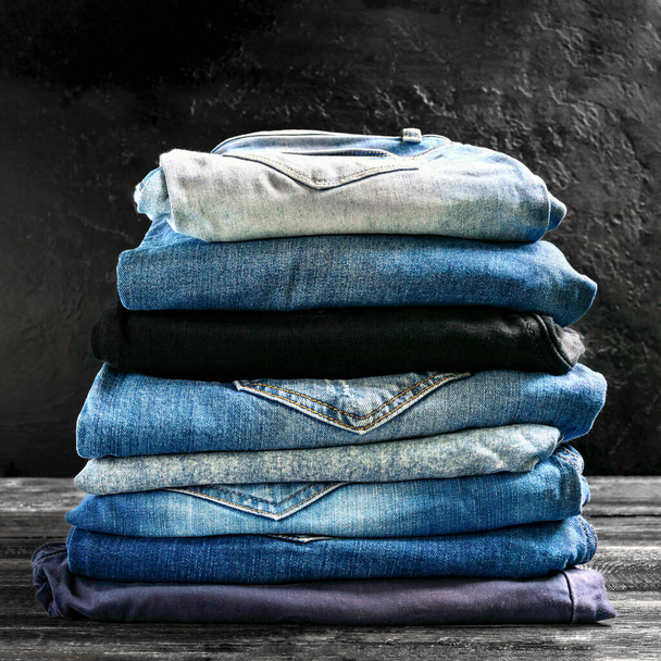 Много разных джинсов в стопке на столе. Концепция популярной, удобной одежды. - Фото, изображение