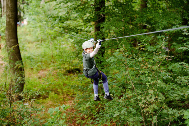 Orman macera parkındaki okul çocuğu. Aktif çocuk, kask takan çocuk yüksek ip izine tırmanıyor. Çeviklik becerileri ve çocuklar için açık hava eğlence merkezine tırmanma. Çocuklar ve aileler için açık hava aktivitesi. - Fotoğraf, Görsel