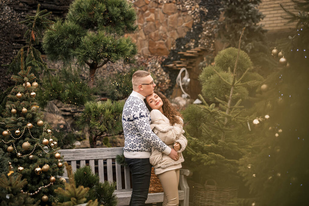 Χριστουγεννιάτικα κλαδιά ελάτης. Νεαρό ζευγάρι διακοσμεί ένα χριστουγεννιάτικο δέντρο έξω. Χριστουγεννιάτικα στολίδια, γλειφιτζούρια και μπάλες. - Φωτογραφία, εικόνα