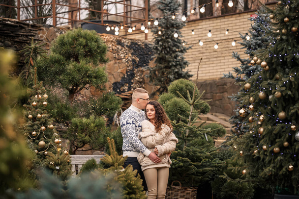 Christmas tree fir branches. Young couple decorating a Christmas tree outside. Christmas decorations, lollipops and balls. - Foto, afbeelding