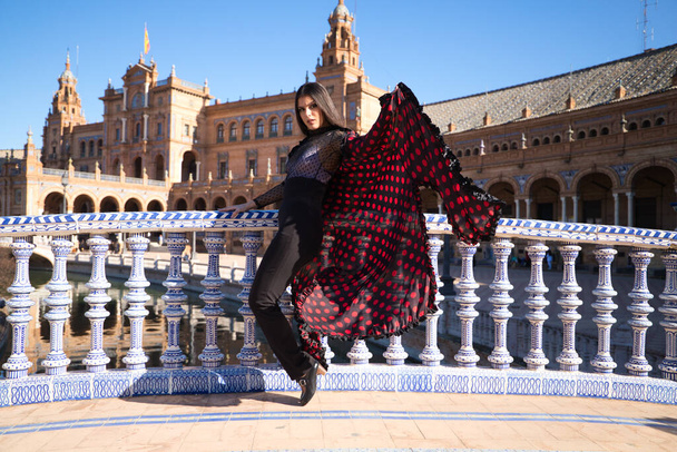 Young and beautiful woman dancing flamenco and Spanish posing in urban clothes, wearing her hair loose and long and standing on the tips of her shoes. flamenco cultural heritage of humanity. - Fotó, kép