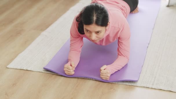 Азиатка, занимающаяся доской для йоги дома во время пандемии COVID-19, занимается спортом в гостиной. - Кадры, видео