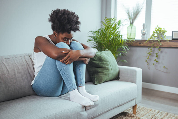 Frustrated young lady sitting on sofa, cuddling pillow, looking away at window. Lost in thoughts unhappy stressed millennial woman regretting of wrong decision, spending time alone in living room. - Foto, Imagen
