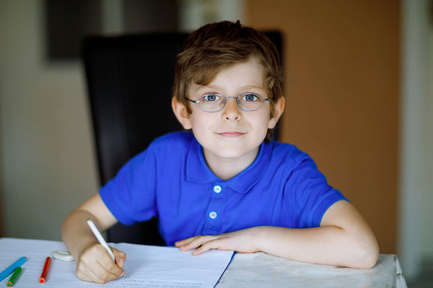 Portrait of little kid boy with glasses at home making homework, writing letters with colorful pens. Little child doing exercise, indoors. Elementary school and education, home schooling concept. - Фото, изображение