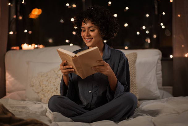 happy woman reading book sitting in bed at night - Photo, Image
