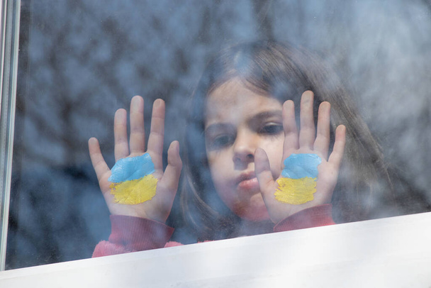 Pieni tyttö ikkunassa talonsa maalattu keltainen-sininen lippu Ukrainan, rauha Ukrainassa, lopettaa sodan, protesti ja patriootti, koti Ukraina - Valokuva, kuva
