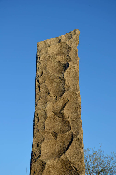 la colonne de granit est battue en pierre avec des copeaux grossiers rappelant la production préhistorique de lances à partir d'obsidiens siliceux. stèle grise ciel bleu. monument ou pierre tombale - Photo, image