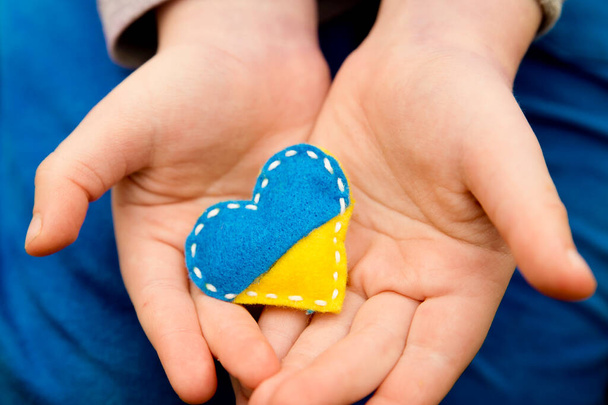 Tema bandera de Ucrania. Insignia de pin en forma de corazón hecha de fieltro de peluche azul y amarillo en la mano del niño. Asuntos tópicos de la guerra. Luchadores por la libertad. Apoyo a las naciones, unidad - Foto, imagen