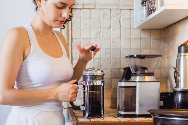 fiatal kaukázusi nő az otthoni konyhájában kávét készít egy kézi francia sajtó kávéfőző a pulton, kávézó és életmód koncepció. - Fotó, kép