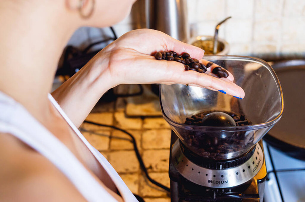 close-up de jovem caucasiana na cozinha derramando grãos de café em um moedor elétrico no balcão, estilo de vida e conceito da indústria do café - Foto, Imagem