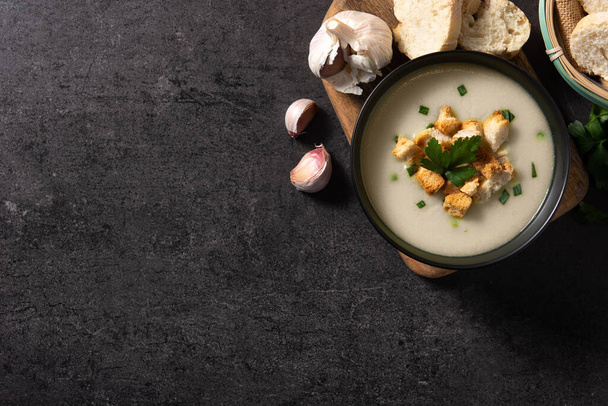 Garlic soup topped with croutons in bowl on black slate background. Top view. Copy space - Foto, Imagen