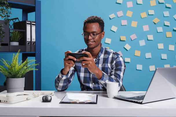Empresário afro-americano jogando jogos no smartphone móvel enquanto no escritório moderno do espaço de trabalho. - Foto, Imagem