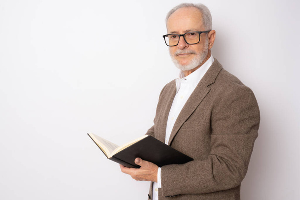 Портрет пожилого человека в элегантной одежде, читающего книгу, стоящую на белом фоне. - Фото, изображение