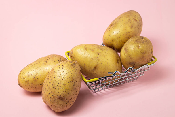 Jeunes pommes de terre dans un panier sur fond rose. Pommes de terre jaunes crues. Nouvelle culture - Photo, image