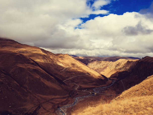Rzeka węża płynie w wąwozie górzystej jesiennej doliny. Droga węzłowa i most przez rzekę w wysokich górach Kaukazu - Zdjęcie, obraz