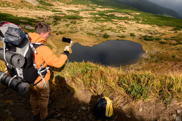 Турист сидить на траві високо в горах на задньому плані озера Несамовит, турист і озеро Несамовит, туристичний блог на мобільному телефоні з стабілізатором.. - Фото, зображення