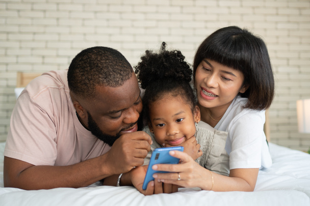 Rodzina bawi się i gra w gry edukacyjne online ze smartfonem w domu w sypialni. Pojęcie edukacji online i opieki ze strony rodziców. - Zdjęcie, obraz