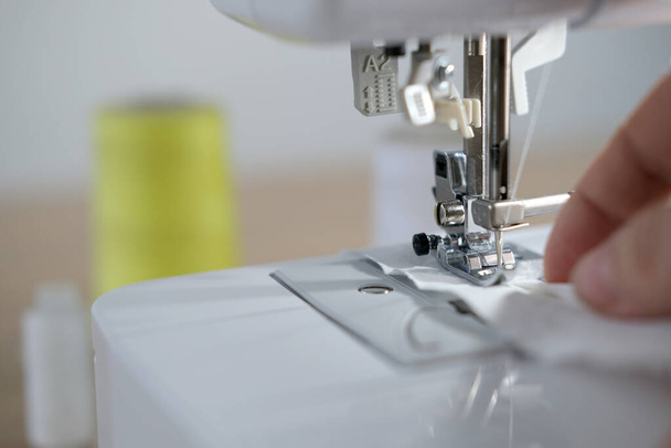 close-up of female hands perform work on a white sewing electric computer machine, stitches appear step by step on the fabric, concept of tailoring, women's hobby, modern needlework - 写真・画像