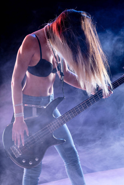 Divatos hipster női zenész elektromos gitározik a színpadon, füstös hangulatban, hosszú hajjal az arcán. - Fotó, kép