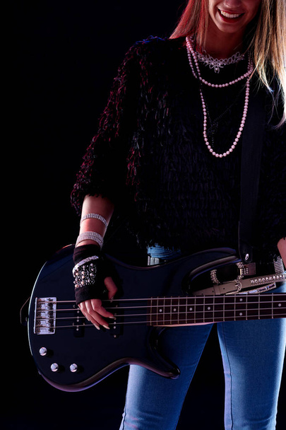 Young female musician in chic outfit performing on stage posing with her electric guitar in a close up portrait cropped to her smile - Photo, Image