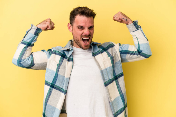 Young caucasian man isolated on yellow background showing strength gesture with arms, symbol of feminine power - Photo, Image