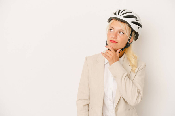 若いですビジネスロシアの女性を保持しています自転車ヘルメット白い背景に隔離されました横に見えます疑いと懐疑的な表情. - 写真・画像