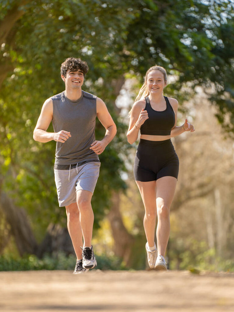 Νεαρό ζευγάρι κάνει σπορ τρέχει σε ένα μονοπάτι πάρκο και χαμογελώντας - Φωτογραφία, εικόνα