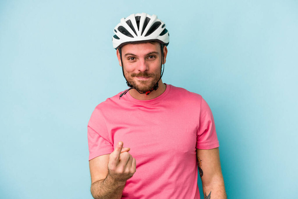 Nuori valkoihoinen mies pyöräilykypärä eristettynä sinisellä taustalla osoittaen sormella sinua ikään kuin kutsuva tule lähemmäksi. - Valokuva, kuva