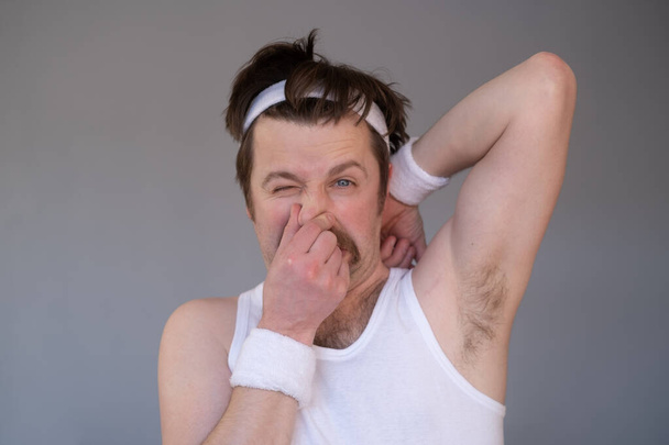 Caucasian sportsman with retro mustache sniffs his sweaty armpit in disgust - Photo, Image