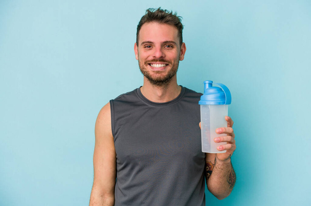 Young caucasian man drinking milkshake isolated on  blue background happy, smiling and cheerful. - Foto, imagen