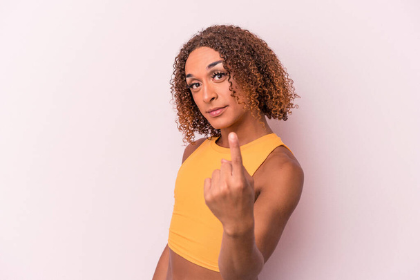 Young latin transsexual woman isolated on pink background pointing with finger at you as if inviting come closer. - Foto, Imagen
