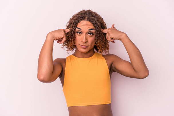 Junge lateinamerikanische transsexuelle Frau isoliert auf rosa Hintergrund konzentriert sich auf eine Aufgabe und hält Zeigefinger auf den Kopf. - Foto, Bild