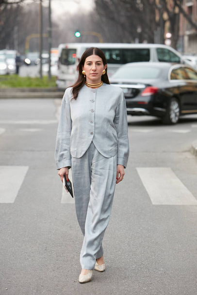 MILAN, ITALY - FEBRUARY 24, 2022: Woman with cold gray jacket and trousers with square pattern and golden necklace and earrings before Emporio Armani fashion show, Milan Fashion Week street style - Foto, Imagen