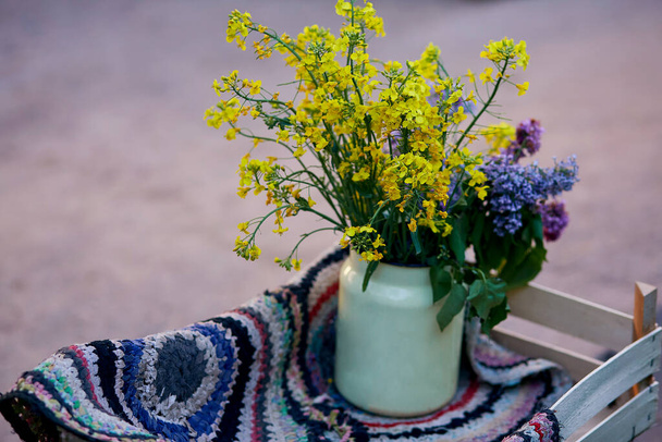 Vintage colorful handmade rug and yellow spring flowers in watering can. Country life, cottage core, creative rustic patchwork concept - Photo, Image
