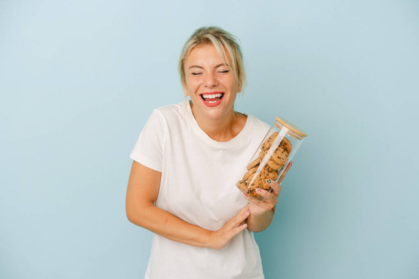 jong russisch vrouw het houden van een koekjes geïsoleerd op blauwe achtergrond lachen en plezier. - Foto, afbeelding