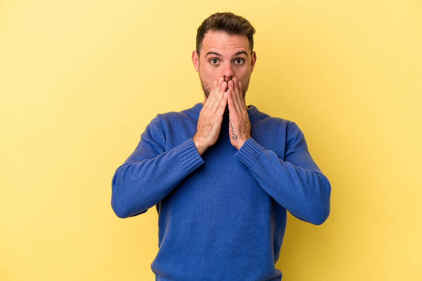 Young caucasian man isolated on yellow background shocked covering mouth with hands. - Φωτογραφία, εικόνα
