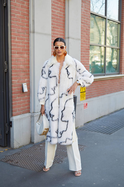 MILAN, ITALIE - 23 FÉVRIER 2022 : Femme avec manteau en fourrure avec silhouette noire et pantalon blanc avant le défilé de mode Fendi, Milan Fashion Week street style - Photo, image