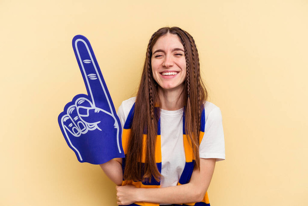 Young sports fan woman isolated on yellow background laughing and having fun. - Photo, Image