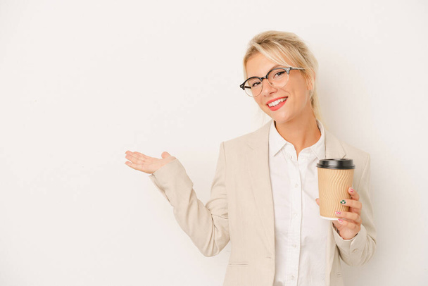 Junge Geschäftsfrau russische Frau hält Take-away-Kaffee isoliert auf weißem Hintergrund zeigt eine Kopie Raum auf einer Handfläche und hält eine andere Hand auf der Taille. - Foto, Bild