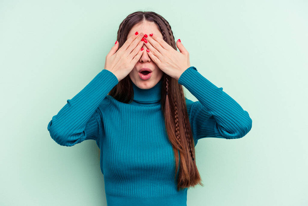jonge Kaukasische vrouw geïsoleerd op groene achtergrond bang bedekken ogen met handen. - Foto, afbeelding