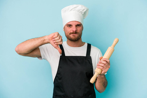 Jeune boulanger isolé sur fond bleu montrant un geste détestable, pouces baissés. Concept de désaccord. - Photo, image