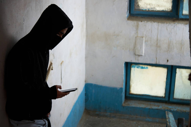 a maniac, robber, a man in a black hood is standing on the stairs, using the phone. - Photo, Image