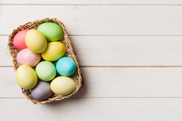 Huevos de Pascua multicolores en la cesta tejida sobre fondo de color. Huevos de Pascua color pastel. concepto de vacaciones con espacio de copia. - Foto, Imagen