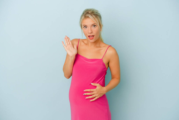 Young Russian woman pregnant isolated on blue background surprised and shocked. - Фото, изображение