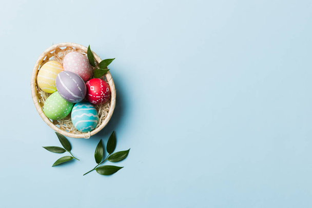 Vícebarevné velikonoční vajíčka v tkané koše na barevném pozadí. Pastelová barva Velikonoční vejce. dovolená koncept s kopírovacím prostorem. - Fotografie, Obrázek