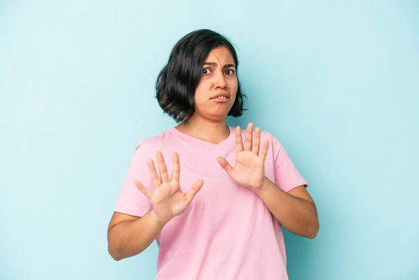 Jonge latijnse vrouw geïsoleerd op blauwe achtergrond verwerpen iemand die een gebaar van walging tonen. - Foto, afbeelding