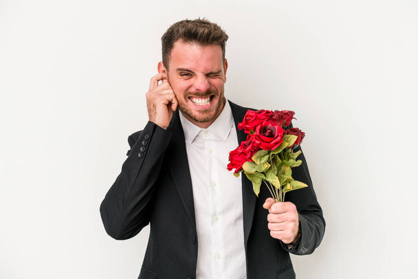 Young caucasian man holding bouquet of flowers isolated on white background covering ears with hands. - Photo, Image